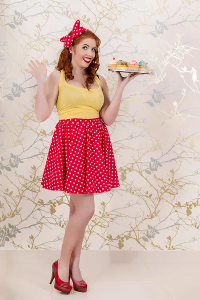 Bella pinup rossa ragazza che tiene un vassoio di cupcake colorati — Foto Stock