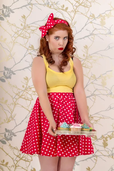 Belle fille rousse pinup tenant un plateau de cupcakes colorés — Photo