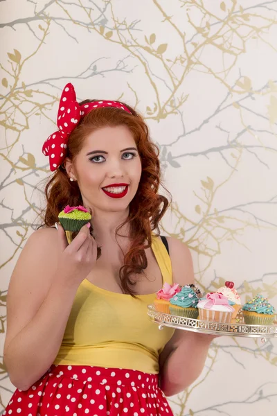 Belle fille rousse pinup tenant un plateau de cupcakes colorés — Photo