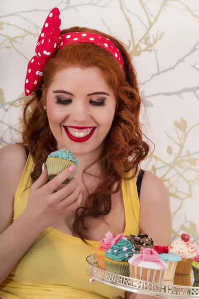 Vackra pinup rödhårig flicka håller en bricka med färgglada cupcakes — Stockfoto