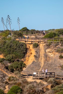 LAGOS, PORTUGAL - 23 Ekim 2021: Portekiz, Lagos 'un sahil şeridi kayalıkları yakınlarındaki tahta tahta kaldırımda yürüyen turistler.