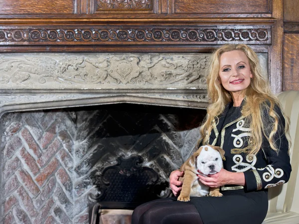 Woman sitting by a fireplace with a dog puppy — Stock Photo, Image