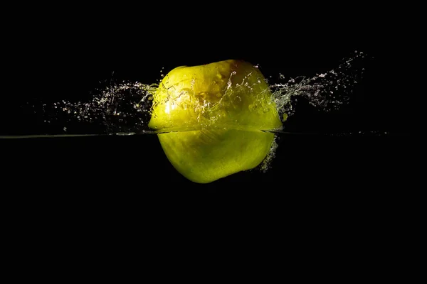 Green apple falling into the water with a splash on a black background closeup