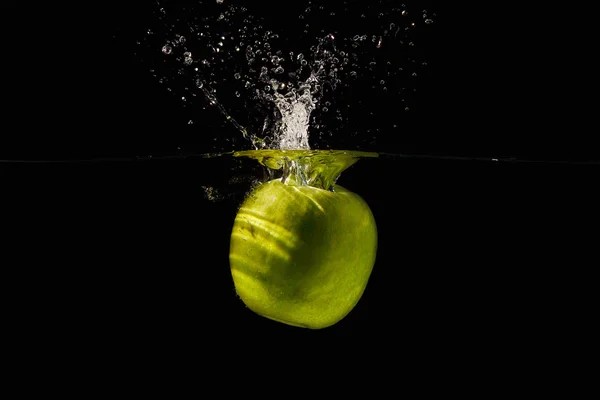 Ripe green apple falling into the water with a splash on a black background closeup