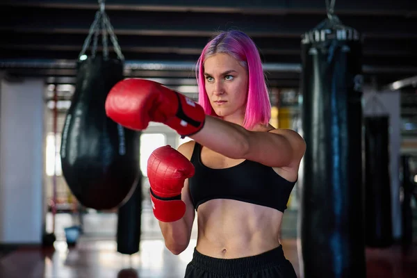 Chica atractiva con guantes de boxeo y ropa ajustada en la práctica