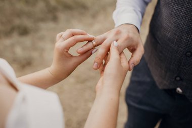 Düğün töreninde, gelin nikah yüzüğünü damadın parmağına takar. Yüzüklü yeni evlilerin elleri. Heteroseksüel genç çift düğünlerinin tadını çıkarıyor.