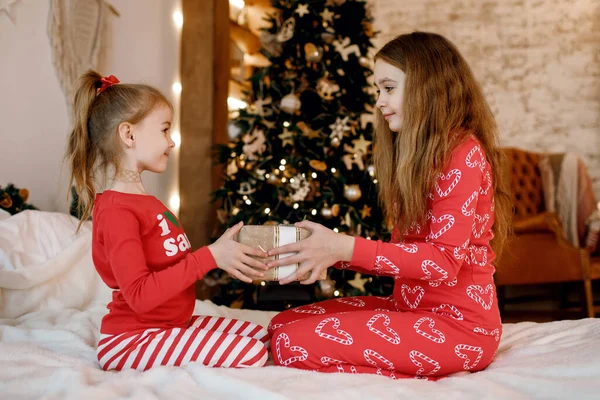 Två Systrar Röd Pyjamas Sitter Sängen Och Håller Gåva Dekorerad — Stockfoto