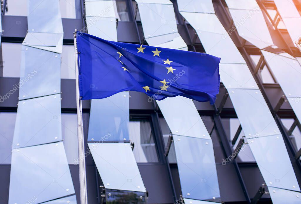 EU flag on the background of a glass office building with a geometric unusual design in blue. Symbol of European countries united in one democratic union