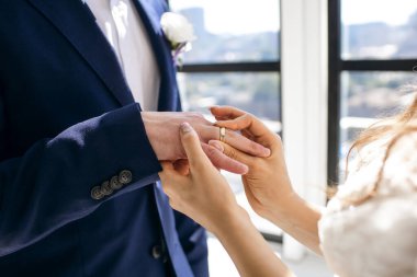 Kapalı bir nikah töreninde gelin nikah yüzüğünü damadın parmağına takar. Yüzüklü yeni evlilerin elleri yakın plan. Altın yüzüklerle geleneksel düğün töreni