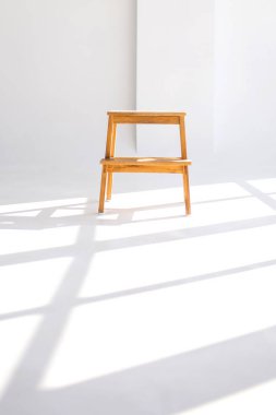 Pencereleri gölgeli beyaz bir odada yalnız bir tahta sandalye. Küçük mobilyaları olan minimalist bir tarz. Temiz beyaz zemindeki pencerelerin gölgesi. Yalnızlık kavramı