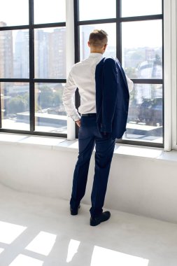 Mavi takım elbiseli ve beyaz gömlekli bir adam pencerenin yanında duruyor ve şehre bakıyor. Bir işadamı ofisinden sokağa bakar. Müdür pencereden dışarı bakar ve haftasonunun hayallerini kurar.