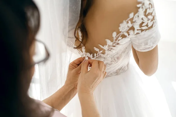 ママは花嫁が白いウェディングドレスをボタンアップするのを助ける 花嫁のドレスを閉じる上で母の手とボタン 花嫁は彼女の結婚式のドレスを着ると新郎を満たすために準備 — ストック写真
