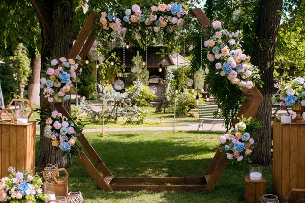 Wooden arch in the form of a hexagon for a wedding ceremony. The wedding arch is decorated with bright flowers and lights in the form of a garland. Beautiful wedding decor for a wedding ceremony