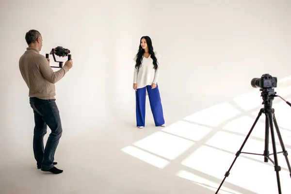 A woman blogger shoots a video blog in a studio with the help of a videographer with two professional video cameras. Modern work as a blogger or journalist for your subscribers