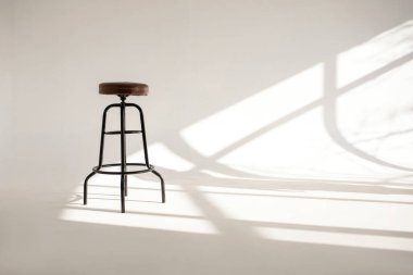 Pencereden güneşten gölgeli beyaz bir oda ve yüksek bir bar taburesi. Bu tarz, yatay fotoğrafçılıktaki minimalizm. Tek sandalyeli ve beyaz boşluklu yalnızlık kavramı