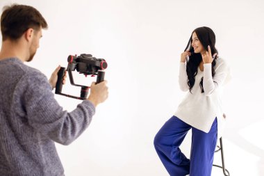 Bir kadın blogcu profesyonel bir video kamerayla stüdyoda video blogu çekiyor. Blog yazarı ya da gazeteci olarak modern bir çalışma. Esmer, saçlarını düzleştiriyor.