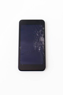 Beyaz arka planda kırık ekranlı siyah cep telefonu. Yere düştükten ya da vurulduktan sonra ekranı tamamen kırılmış siyah bir akıllı telefon çalışmıyor ve onarılması gerekiyor.