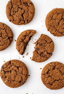 Beyaz arka planda çikolatalı kurabiyeler. Lezzetli ev yapımı çikolatalı kurabiyeler beyaz arka planda güzelce serilmiş. Dikey fotoğrafta çatlak kurabiyeler ve kırıntılar