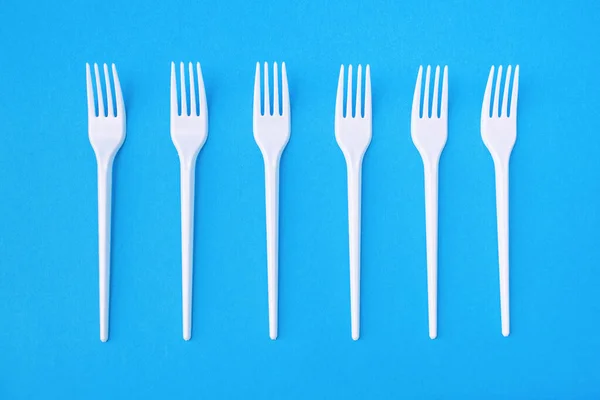 Six plastic forks on a blue paper background for single use. Dangerous plastic for the environment. Disposable eating utensils