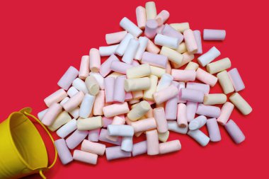 Kırmızı arka planda küçük sarı bir kova ve bir sürü rengarenk marşmelov. Çökmüş şekerleme konsepti. Lezzetli tatlı ya da içeceklere ilave