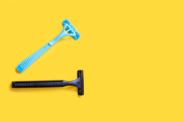 Sarı izole edilmiş arka planda siyah ve mavi renkte iki plastik tıraş bıçağı. Erkek ve kadın tek kullanımlık tıraş bıçağı ve yazı için boş yeri var. Görünüm ve pürüzsüz cilt bakımı kavramı