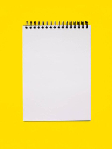 Notebook made of white paper with binding on a yellow background. Blank notepad with free space for text. Notebook in classic binding without notes on vertical photo
