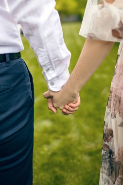 Bir adam ve bir kadın yeşil bir çimenliğin arka planında el ele tutuşuyorlar. Beyaz gömlek ve siyah pantolon giymiş bir adam elbise giymiş bir kadının elini tutuyor. Güçlü ilişkiler kavramı