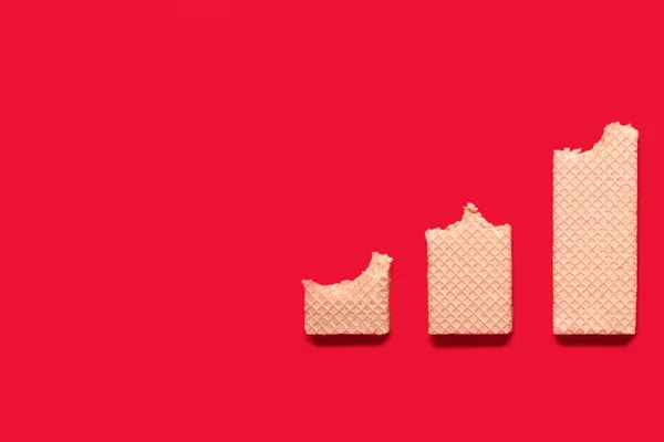 減少グラフの形で赤い背景にビッテンワッフル サクッとしたワッフルの形でお菓子を食べるというコンセプト テキストと広告のための無料スペース おいしい甘いデザート — ストック写真