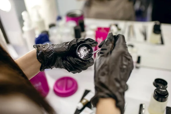 Eyebrow master smears a brush with eyebrow paint in a beauty salon close-up. A set of tools for eyebrow care. Master browist in black gloves