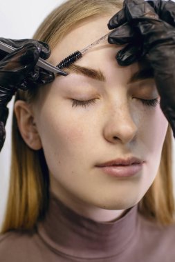 Profesyonel bir kaş ustası, aletleri kullanarak müşterinin tenine cımbızla istenmeyen kılları temizler. Dikey bir fotoğrafta kaş boyama ve şekillendirme