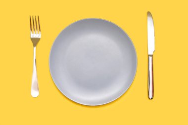 Sarı arka planda çatallı gri tabak ve bıçak. Boş gri tabak ve izole edilmiş sarı arka planda çatal ve bıçak şeklinde tabaklar. Restoran konsepti ya da gıda yerleştirme için boş