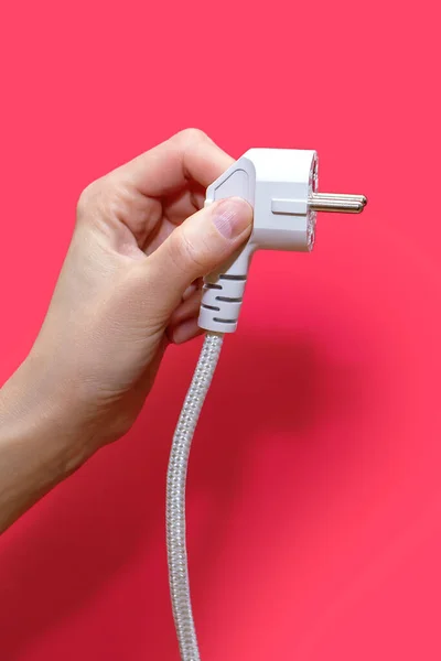 Electric plug for a socket on a pink background. The concept of electricity and its importance in everyday life. Electric plug without socket. Hand holding an electric plug