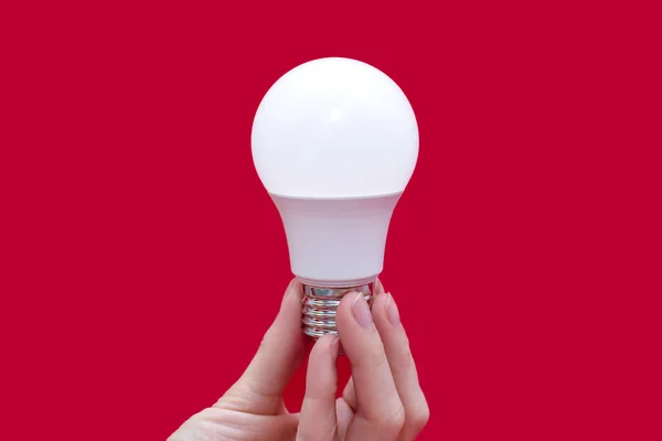 Energy saving light bulb in hand on a red background. Saving energy in everyday human life. Electrical equipment and the evolution of light. Conservation and protection of the environment