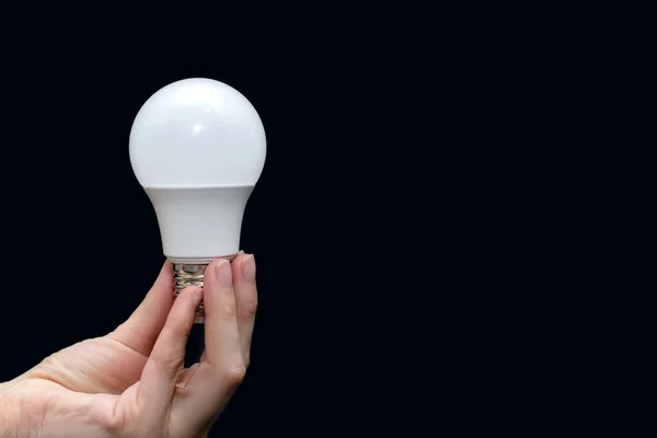 Energy saving light bulb in hand on a black background with free space for text. Saving energy in everyday life. Electrical equipment and the evolution of light. Free space for text and ads