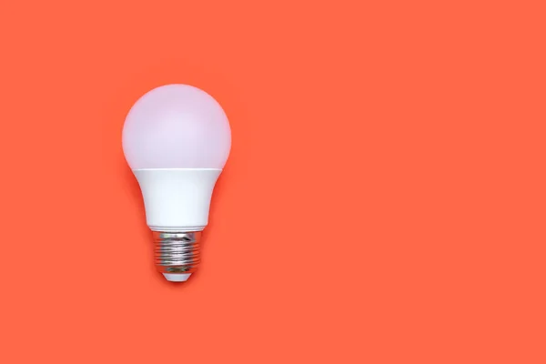 Energy saving light bulb on orange background with free space for text. Saving energy and finances. Electrical equipment and the evolution of light. Free space for text