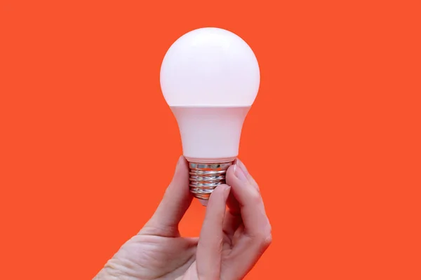 Energy saving light bulb in hand on orange background. Energy saving at home. Electrical equipment and the evolution of light. Conservation and protection of the environment