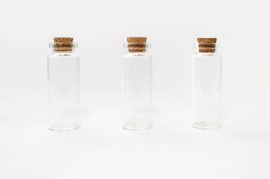 Mantarlı beyaz arka planda üç boş cam şişe. Çeşitli sıvılar için cam kaplar. Birbirinin aynı kapalı test tüpleri.