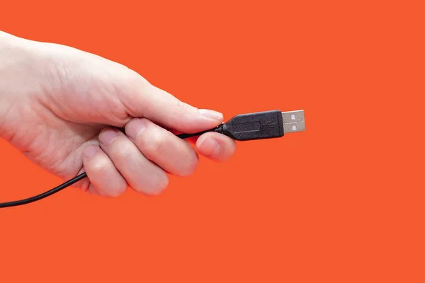 Black USB cable in hand on an orange background. Modern technologies in everyday life. Human hand holding usb cable. Cable for digital transmission of information