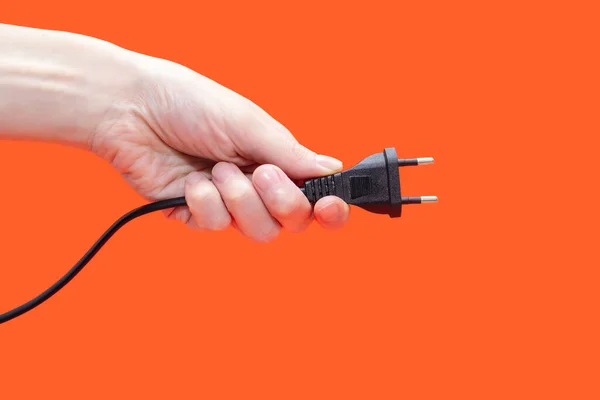 Electric plug for a socket in a hand on an orange background. The concept of electricity and its importance in everyday life. Electric plug without a socket in a human hand. Power plug for the device