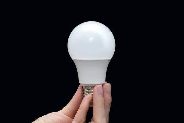 Energy saving light bulb in hand on a black background. Saving energy in everyday life. Electrical equipment and the evolution of light. Preservation and protection of the environment