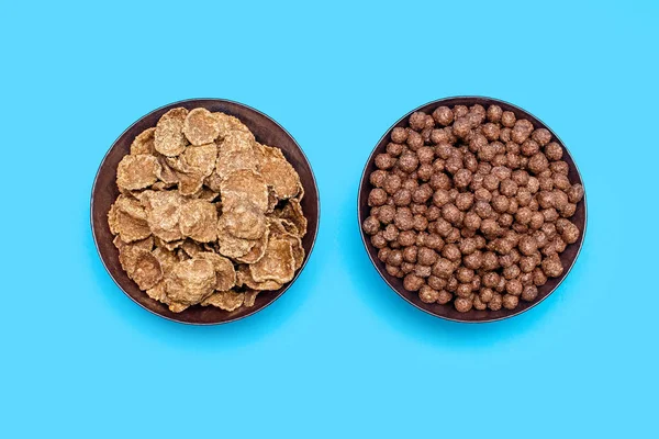 Two types of brown cereals in bowls on a blue background are arranged in a row. Chocolate flakes for preparing a quick energy breakfast rich in carbohydrates