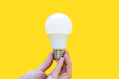 Energy saving light bulb in hand on a yellow background. Energy saving in everyday life. Electrical equipment and the evolution of light. Conservation and protection of the environment