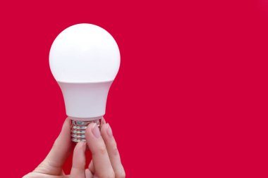 Energy saving light bulb in hand on a red background with free space for text. Saving energy in lighting devices. Electrical equipment and the evolution of light. Free space for text and ads