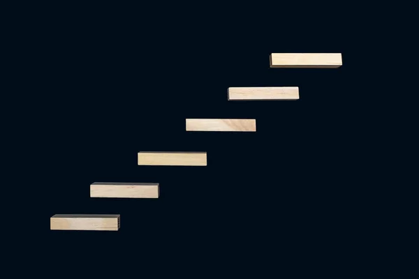 Wooden details lined up in the form of steps on a black background. Wooden rectangles form the shape of steps. The concept of career growth or rise from the bottom to the top