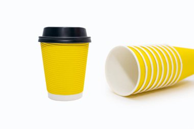 Yellow disposable cardboard cups on a white background. One disposable yellow cup with a plastic lid and a set of clean and ready-to-use disposable cups lie on a white background