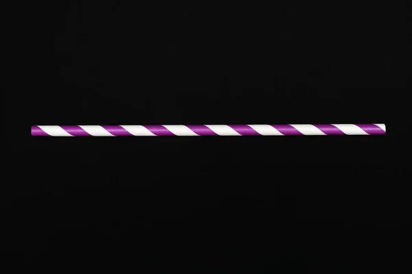 A lilac-white straw is located on a black background. The concept of a children\'s holiday or party. A handy drinking accessory. Eco-friendly paper straw for drinking beverages