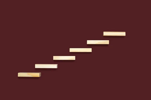 Wooden details lined up in the form of steps on a brown background. Wooden rectangles form the shape of the steps. The concept of career growth or rise from the bottom up