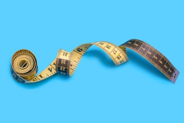 Yellow measuring tape on a blue background. Tool for measuring length and volume. Yellow and black twisted tape for sewing or body measurements