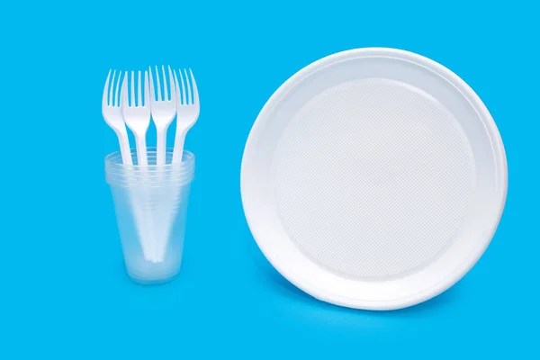 Disposable white plastic tableware in the form of plates, glasses and forks on a blue background. Plastic tableware for a picnic or outdoor party. Plastic pollution and environmental problems