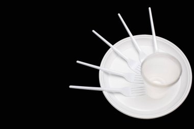 Disposable white plastic tableware in the form of plates, glasses and forks on a black background. Plastic utensils for a picnic or outdoor party. Free space for text